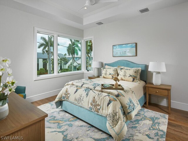 bedroom with ornamental molding, dark hardwood / wood-style flooring, ceiling fan, and a tray ceiling