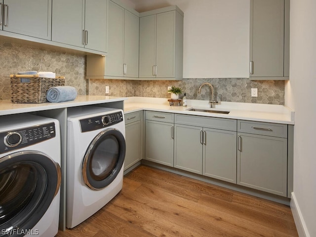 laundry room with sink, washer and clothes dryer, light hardwood / wood-style floors, and cabinets