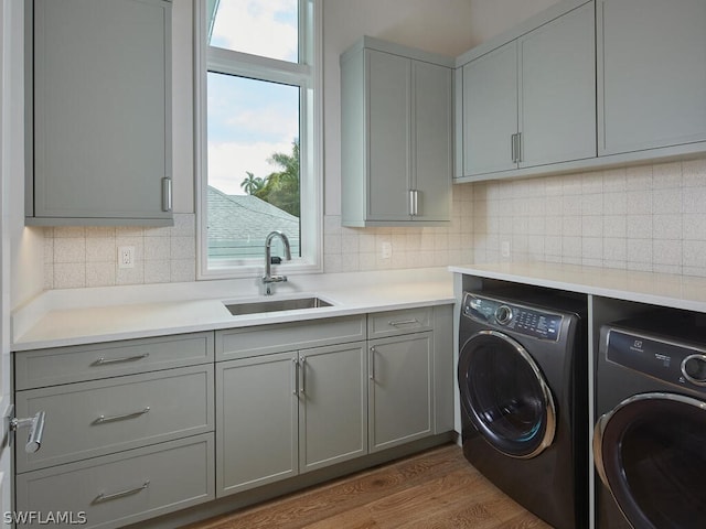 laundry room with sink, wood-type flooring, washing machine and dryer, and cabinets