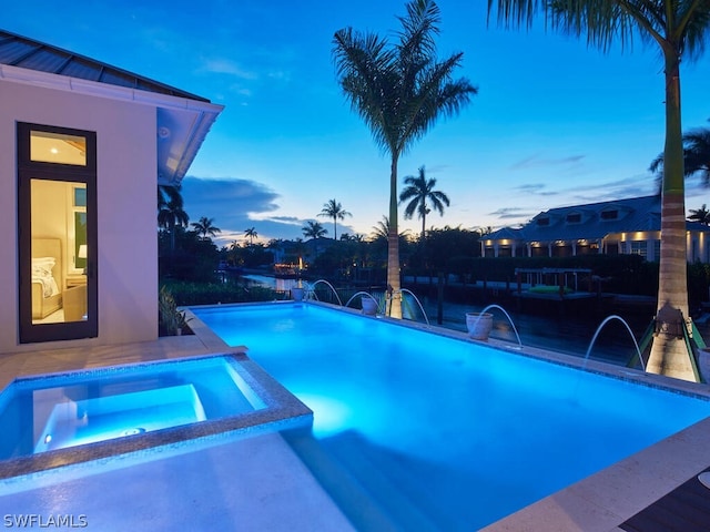 pool at dusk featuring pool water feature and an in ground hot tub