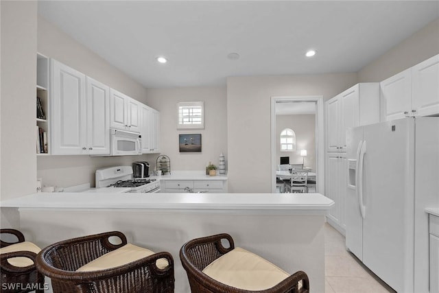 kitchen with kitchen peninsula, a kitchen breakfast bar, white appliances, and white cabinetry