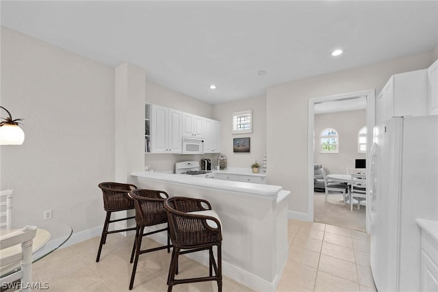 kitchen featuring white appliances, white cabinets, a kitchen breakfast bar, light tile patterned floors, and kitchen peninsula