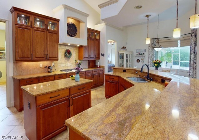 kitchen featuring light stone counters, light tile flooring, hanging light fixtures, a center island with sink, and tasteful backsplash