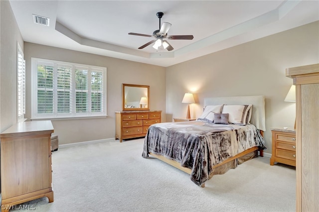 carpeted bedroom with a raised ceiling and ceiling fan