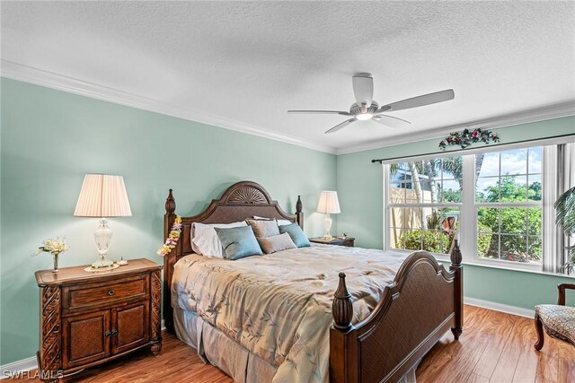 bedroom with ceiling fan, a textured ceiling, ornamental molding, and light wood-type flooring