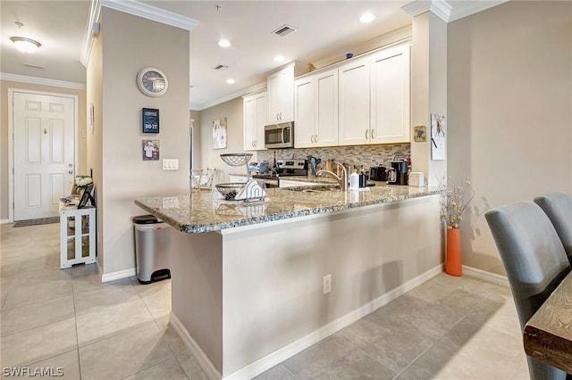 kitchen with kitchen peninsula, appliances with stainless steel finishes, light stone counters, crown molding, and white cabinetry