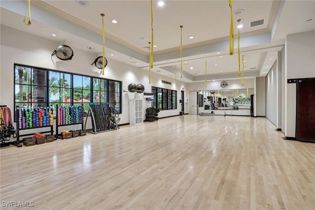 exercise room featuring light wood-type flooring, ornamental molding, and a tray ceiling