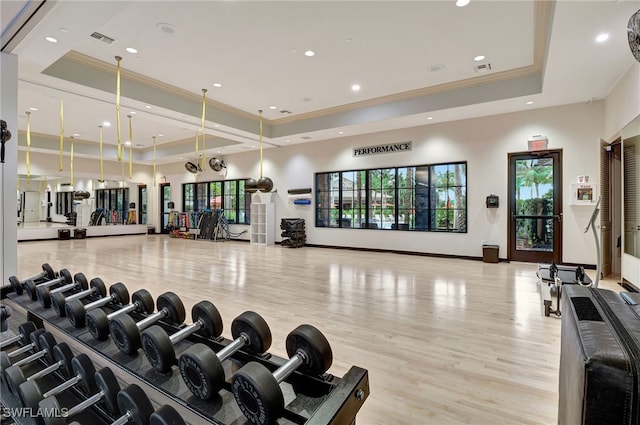 exercise room featuring a raised ceiling, light hardwood / wood-style floors, and ornamental molding