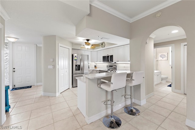 kitchen with a kitchen bar, appliances with stainless steel finishes, light tile patterned floors, and white cabinetry