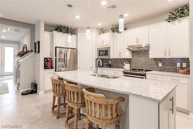 kitchen featuring stainless steel appliances, tasteful backsplash, sink, hanging light fixtures, and a kitchen island with sink