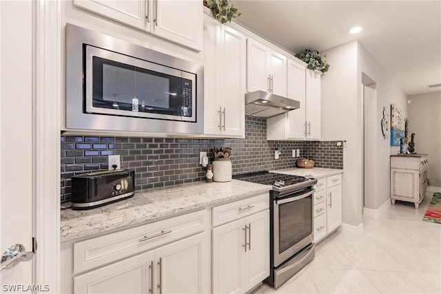 kitchen with tasteful backsplash, white cabinets, light stone counters, and stainless steel appliances