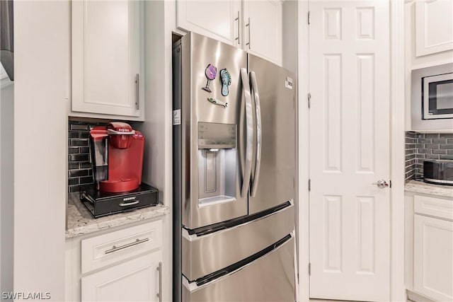 kitchen with appliances with stainless steel finishes, white cabinets, tasteful backsplash, and light stone counters