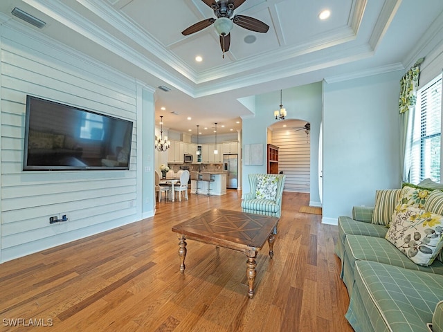 living room with ceiling fan with notable chandelier, crown molding, a tray ceiling, and light hardwood / wood-style flooring