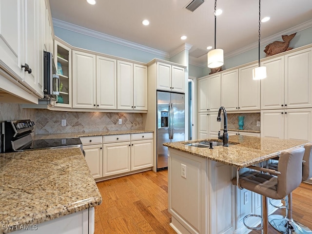 kitchen with a center island with sink, sink, light wood-type flooring, decorative light fixtures, and stainless steel appliances