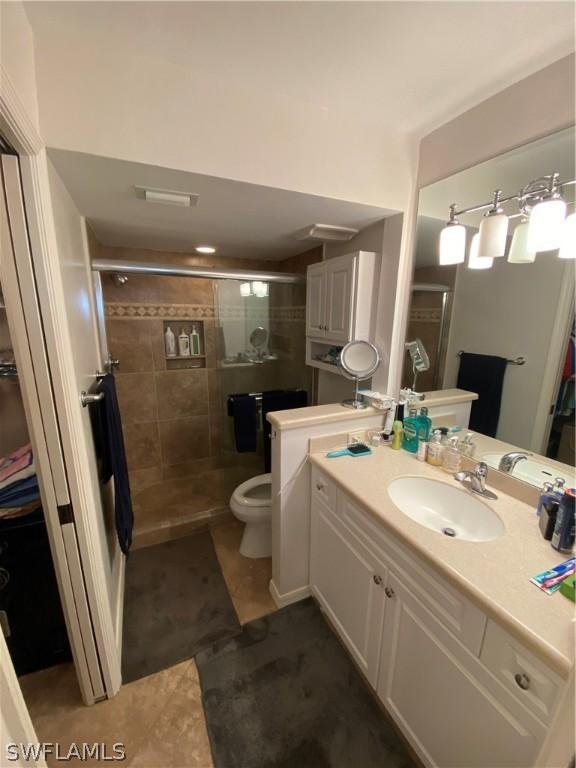 bathroom with a shower with shower door, tile flooring, vanity, and toilet