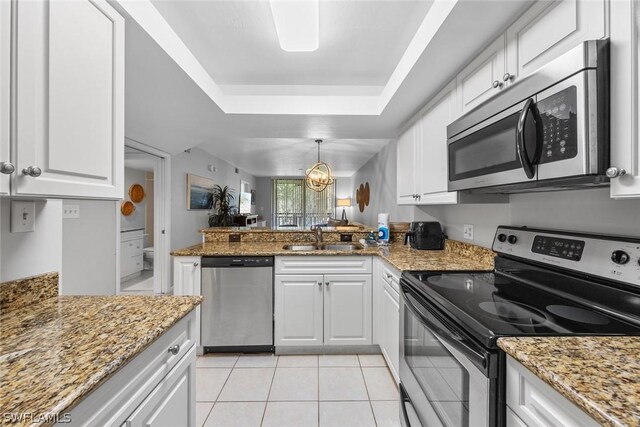 kitchen with a tray ceiling, appliances with stainless steel finishes, white cabinets, a sink, and a peninsula