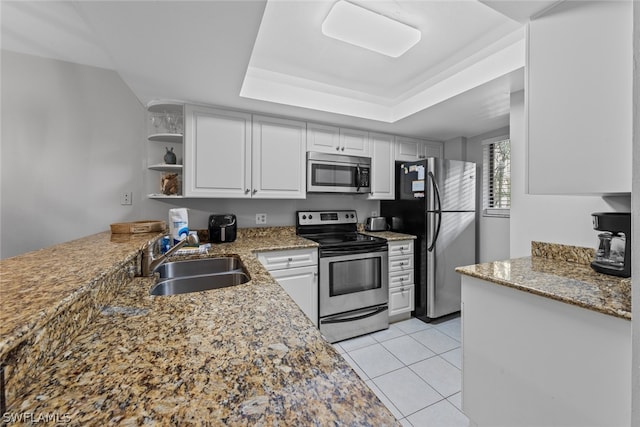 kitchen featuring stainless steel appliances, stone counters, a tray ceiling, sink, and light tile floors