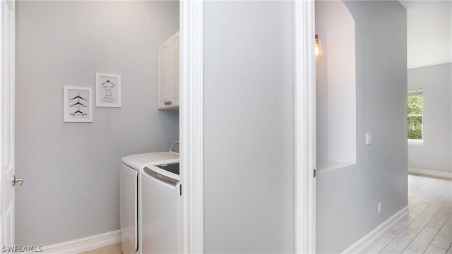 clothes washing area with arched walkways, cabinet space, light wood-style flooring, washer and dryer, and baseboards