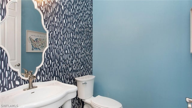 half bathroom featuring a sink, toilet, and wallpapered walls