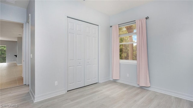 unfurnished bedroom with multiple windows, a closet, and light wood-style flooring