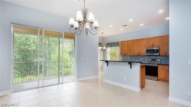 kitchen with tasteful backsplash, dark countertops, appliances with stainless steel finishes, brown cabinets, and a chandelier