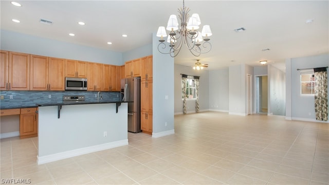 kitchen featuring backsplash, a kitchen island with sink, a breakfast bar, light tile patterned floors, and appliances with stainless steel finishes