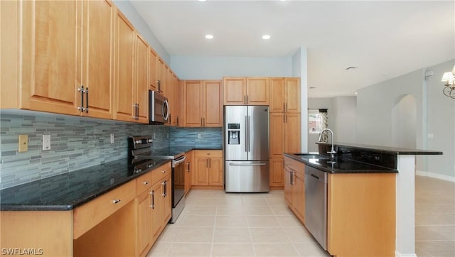 kitchen with light tile patterned floors, stainless steel appliances, decorative backsplash, a sink, and dark stone counters