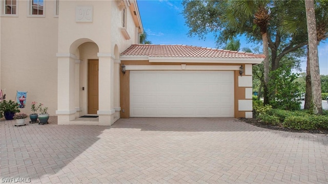 mediterranean / spanish-style house with a tiled roof, decorative driveway, an attached garage, and stucco siding