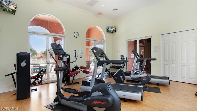 exercise area with ornamental molding, visible vents, a towering ceiling, and baseboards