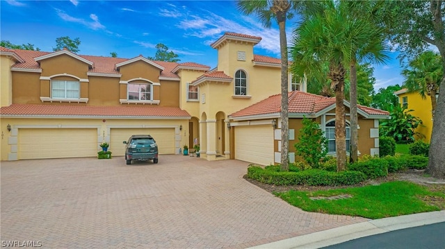 view of front of home with an attached garage, a tiled roof, decorative driveway, and stucco siding