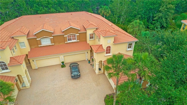 mediterranean / spanish-style house featuring a garage, a tile roof, driveway, and stucco siding