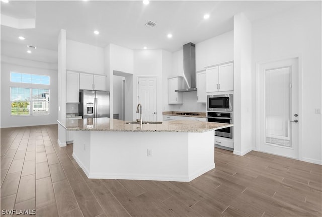 kitchen featuring white cabinetry, stainless steel appliances, wall chimney exhaust hood, and a center island with sink