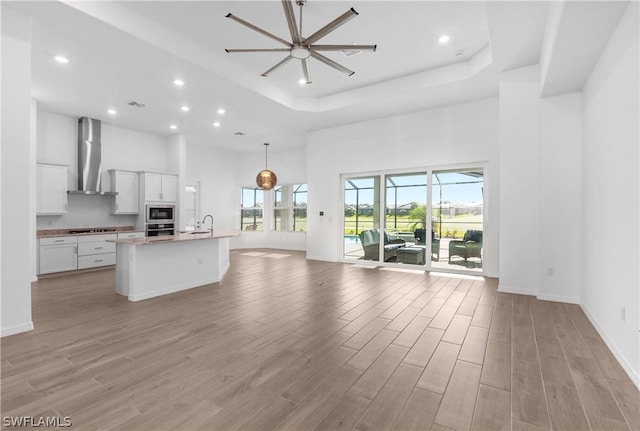 unfurnished living room featuring ceiling fan, a raised ceiling, a high ceiling, and sink