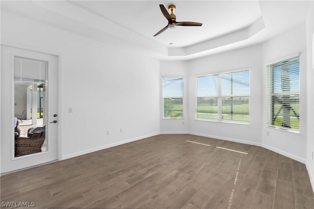 empty room with ceiling fan, dark hardwood / wood-style flooring, plenty of natural light, and a tray ceiling