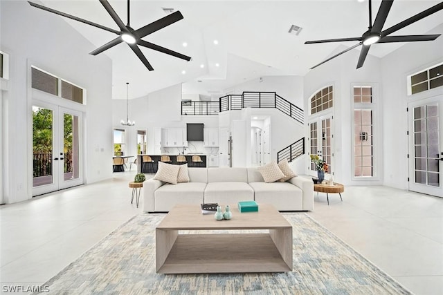 tiled living room featuring ceiling fan with notable chandelier, a towering ceiling, and french doors