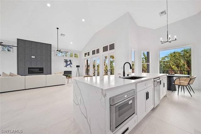 kitchen with pendant lighting, sink, white cabinets, light stone countertops, and an island with sink