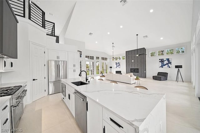 kitchen with white cabinetry, sink, stainless steel appliances, light stone counters, and a large island with sink