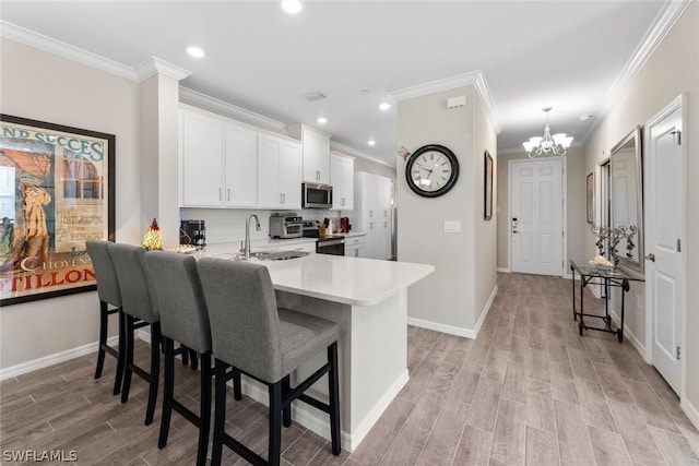 kitchen featuring kitchen peninsula, appliances with stainless steel finishes, ornamental molding, white cabinets, and a breakfast bar area