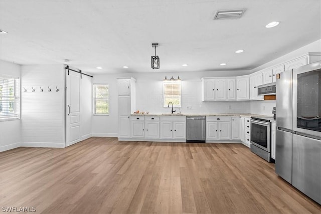 kitchen featuring appliances with stainless steel finishes, decorative light fixtures, white cabinetry, sink, and a barn door