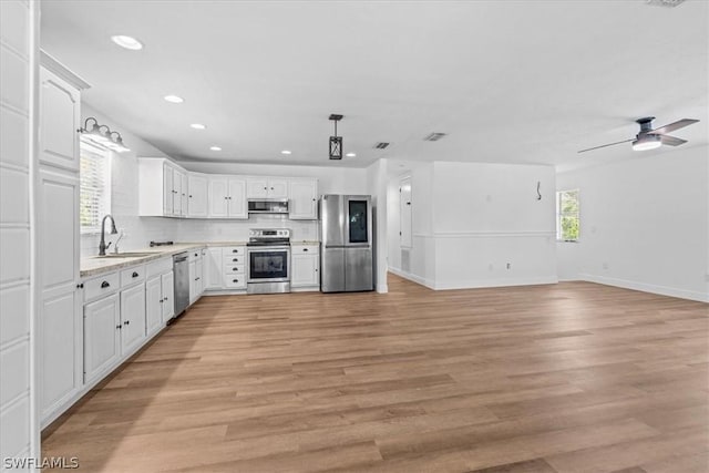 kitchen with appliances with stainless steel finishes, decorative light fixtures, sink, white cabinets, and light hardwood / wood-style flooring