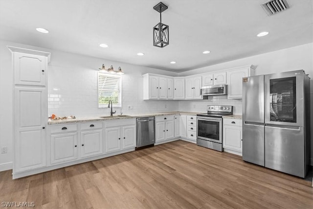 kitchen with appliances with stainless steel finishes, sink, white cabinets, hanging light fixtures, and light hardwood / wood-style floors