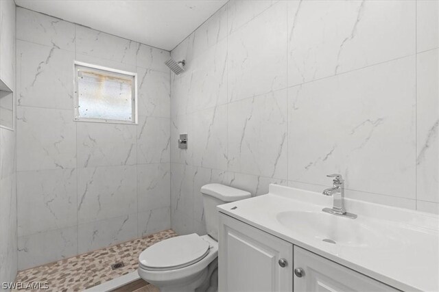 bathroom with a tile shower, tile walls, toilet, and vanity