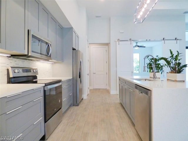 kitchen with a barn door, gray cabinets, appliances with stainless steel finishes, decorative backsplash, and sink