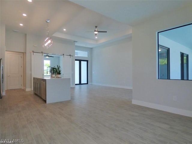 kitchen with ceiling fan, light hardwood / wood-style flooring, a tray ceiling, and pendant lighting