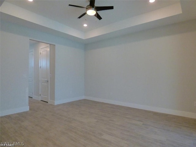 empty room featuring a raised ceiling, ceiling fan, and light hardwood / wood-style flooring