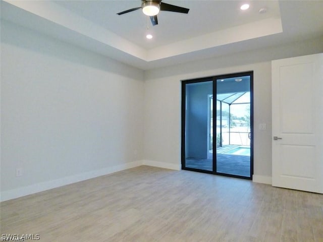 spare room with ceiling fan, a raised ceiling, and light wood-type flooring