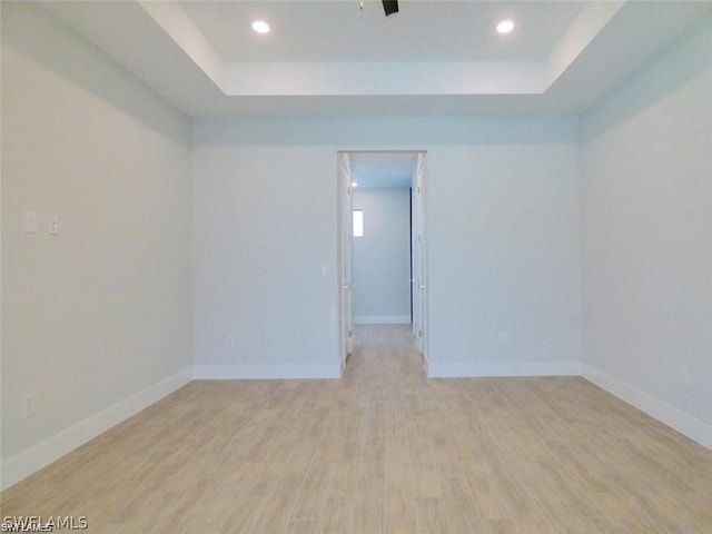 empty room featuring a raised ceiling and light hardwood / wood-style flooring