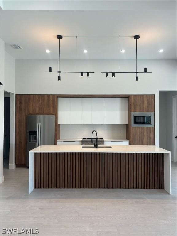 kitchen featuring pendant lighting, sink, a kitchen island with sink, stainless steel appliances, and white cabinets