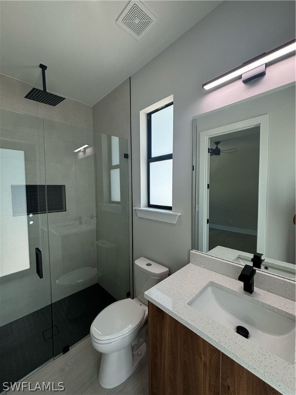 bathroom with a shower with door, toilet, vanity, and ceiling fan