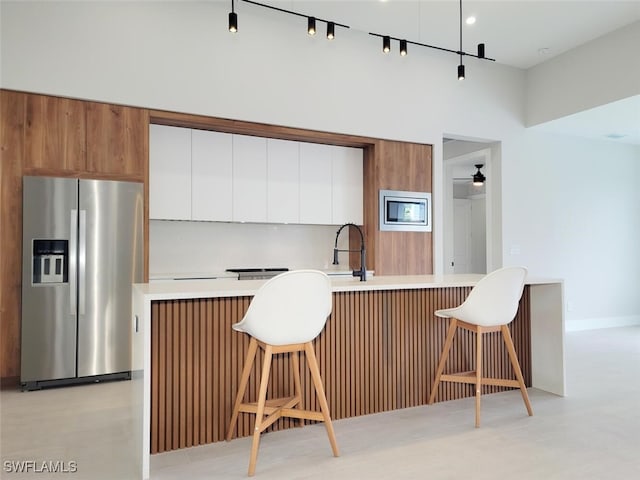 kitchen with appliances with stainless steel finishes, brown cabinets, a breakfast bar area, light countertops, and white cabinetry